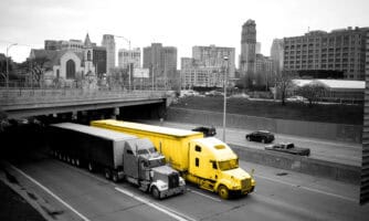 Yellow truck transporting cargo through city highway, emphasizing logistics and freight delivery services.