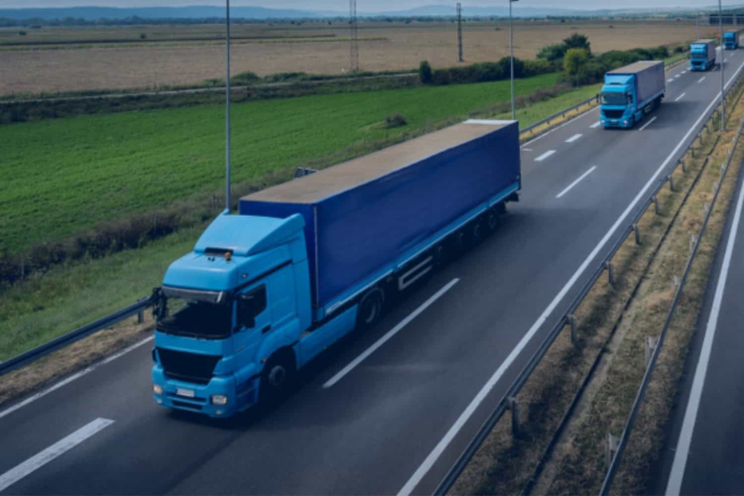 A fleet of over-the-road freight trucks driving single-file