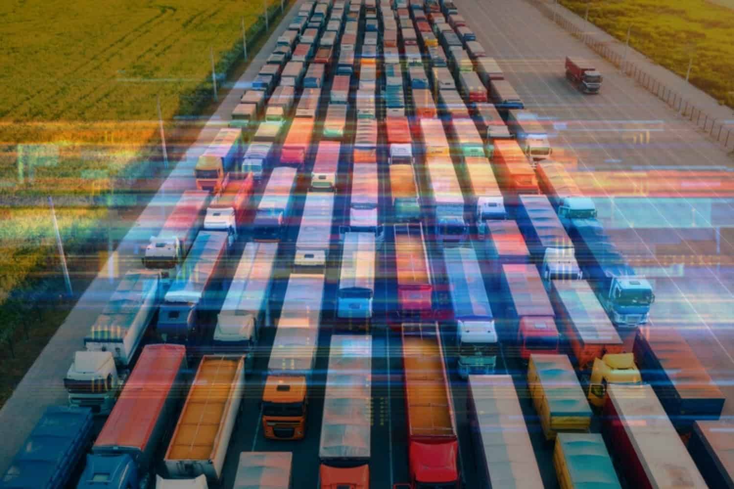 A variety of over-the-road freight trucks driving through a shipping hub