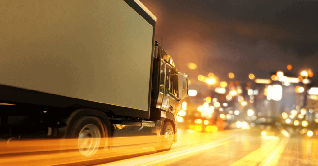 Black delivery truck moving on city street at night with motion blur, representing logistics and supply chain solutions.