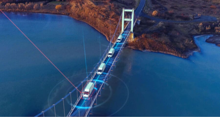 Connected fleet of trucks driving on a high-tech bridge with digital overlay representing IoT and supply chain management for Banyan Technology.