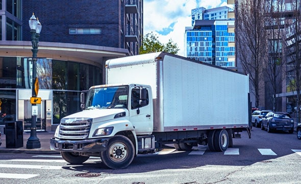 White delivery truck parked on city street near modern office buildings, illustrating efficient logistics and supply chain solutions for businesses.