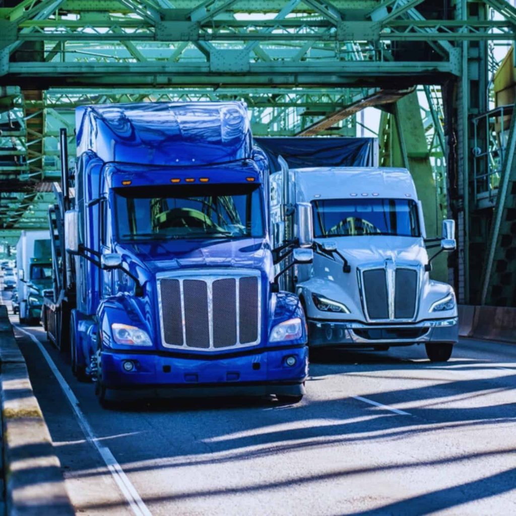 Blue semi-trucks parked under green industrial structure at dockyard for freight transportation.