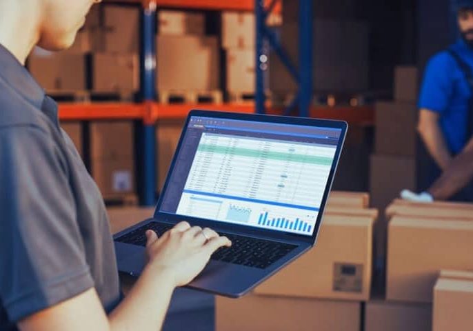Inventory management software on a laptop in a warehouse setting.