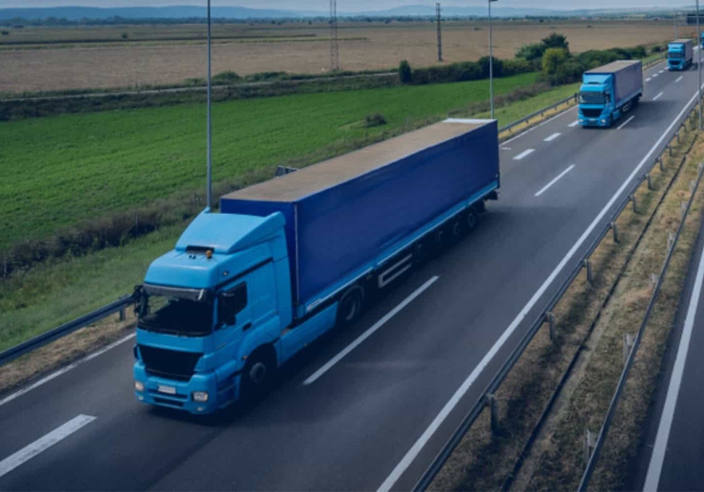 A fleet of over-the-road freight trucks driving single-file